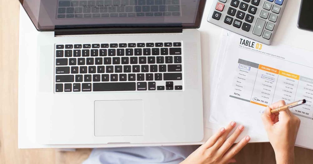 woman calculating managed IT services packages on paper with laptop and computer